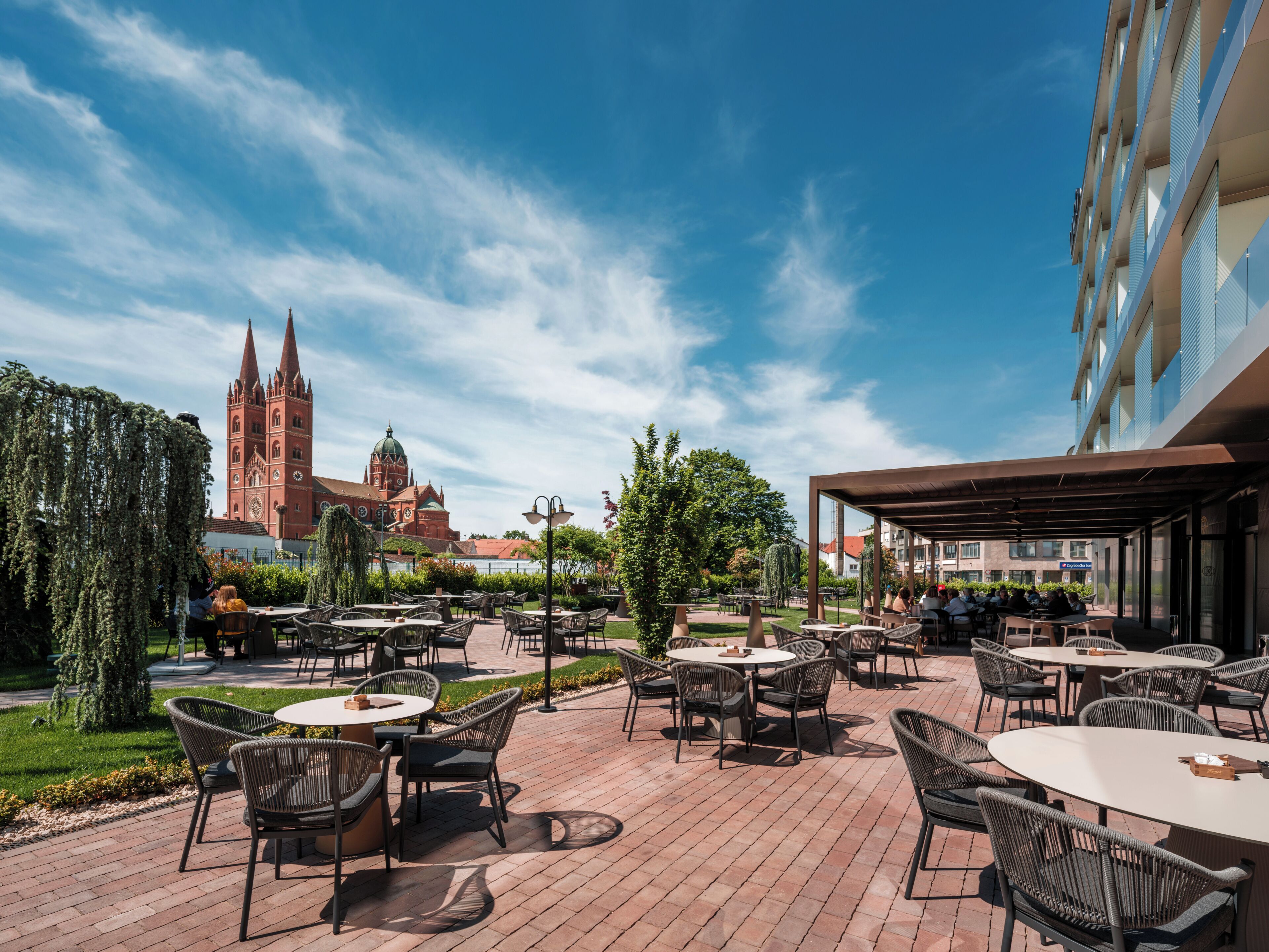 An outdoor patio with round tables and chairs, a church in the background, and a modern building to the right.