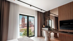 Una habitación de hotel moderna con un ventanal grande, una cama, un escritorio con un ordenador y un televisor.