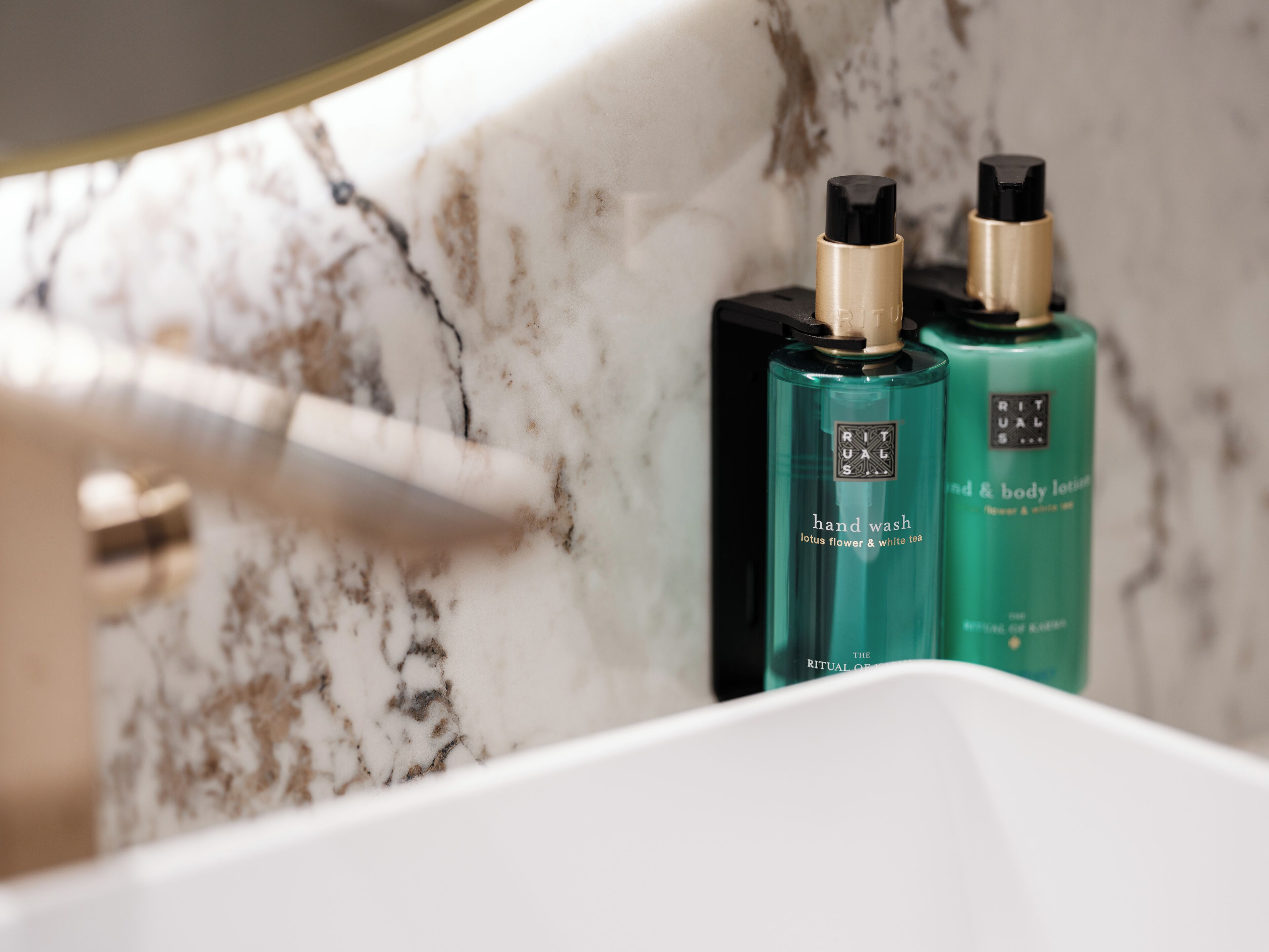 A bathroom with a marble sink, two bottles of hand wash lotion, and a gold-colored faucet.