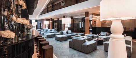 A modern hotel lobby with a central seating area, a reception desk, and a large white lamp.