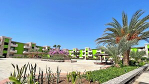 A courtyard with a pool, palm trees, and green buildings. - P22B Cozy & Bright, Steps from the Sea (Santa Maria)