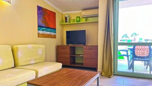 A living room with a sofa, a coffee table, a TV on a wooden cabinet, and a sliding glass door leading to an outdoor area with chairs. - P22B Cozy & Bright, Steps from the Sea (Santa Maria)