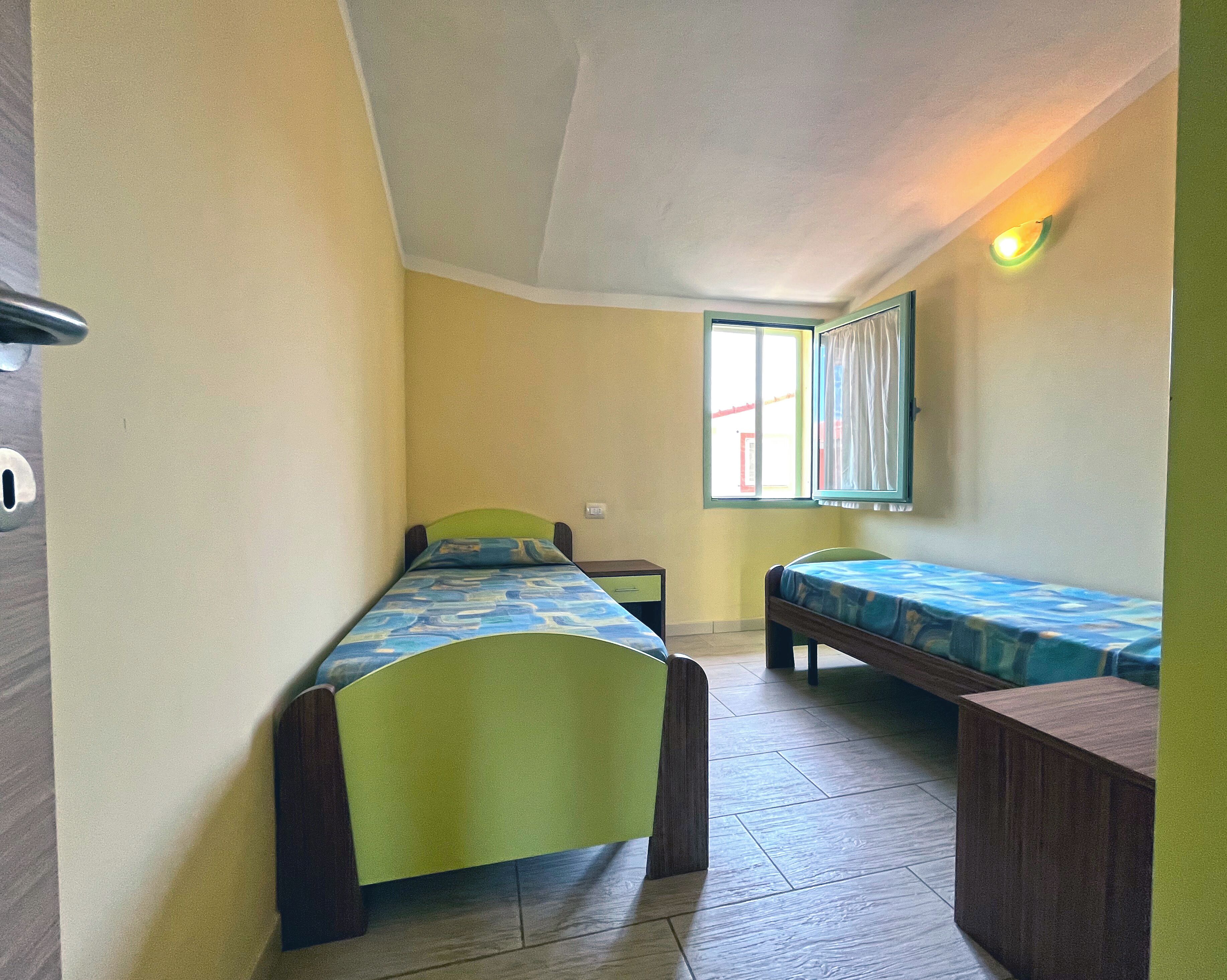 Una habitació petita amb dos llits individuals, una finestra amb cortines i una làmpada penjada a la paret.
