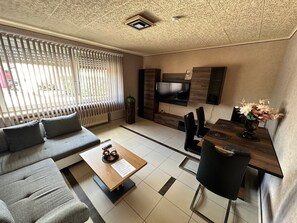 Een moderne woonkamer met een bank, salontafel, televisie en een eethoek.