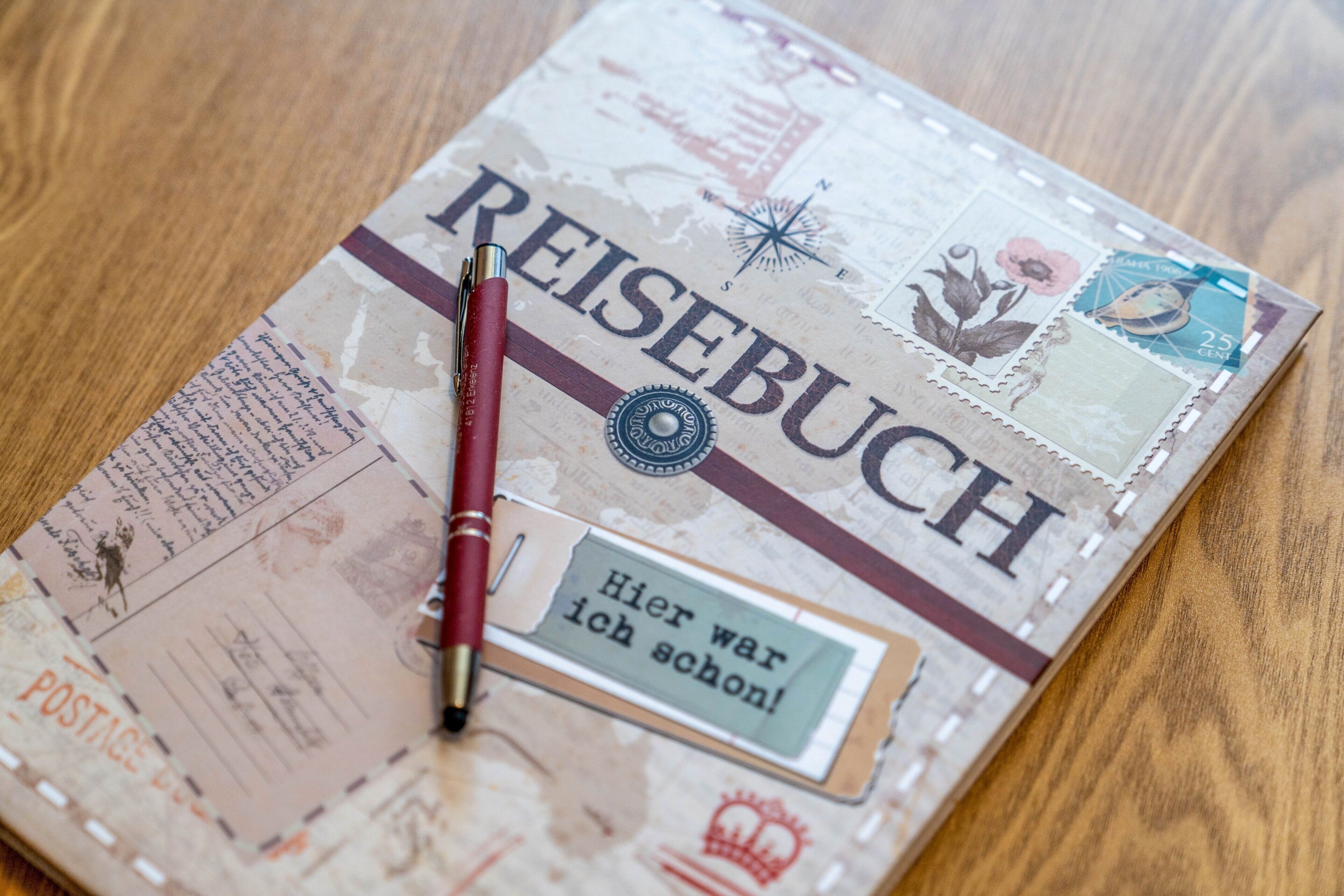 Un carnet avec le mot « REISEBUCH » écrit sur la couverture, une boussole et un stylo.