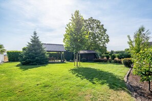 A well-maintained garden with a pergola, a large tree, and a brick building.