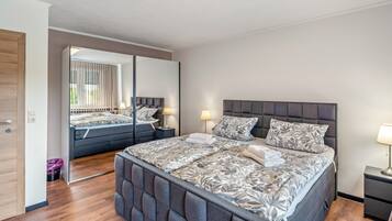 A modern bedroom with a large bed, a nightstand, a mirror, and a wooden door.