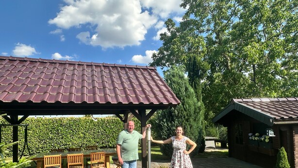 A patio area with a tiled roof, a wooden table with chairs, and a dog.