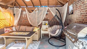 An outdoor patio with a wooden ceiling, a hanging chair, a table with cushions, and a grill. - Apartment "Landleben 2" with Shared Terrace, Private Garden, and Wi-Fi (Erkelenz)