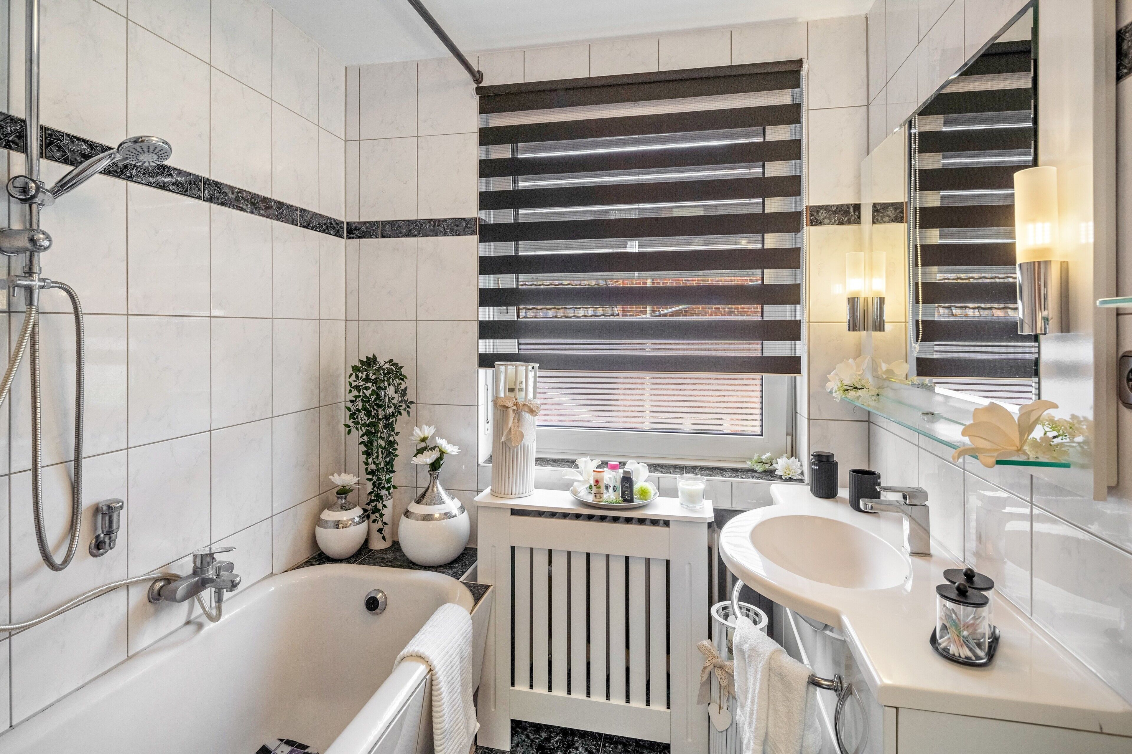 Ein modernes Badezimmer mit einer Badewanne, einer Dusche, einem Waschbecken und einem Fenster mit Jalousien.