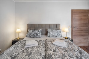 A double bed with floral-patterned bedding, two bedside lamps, and a wooden door.