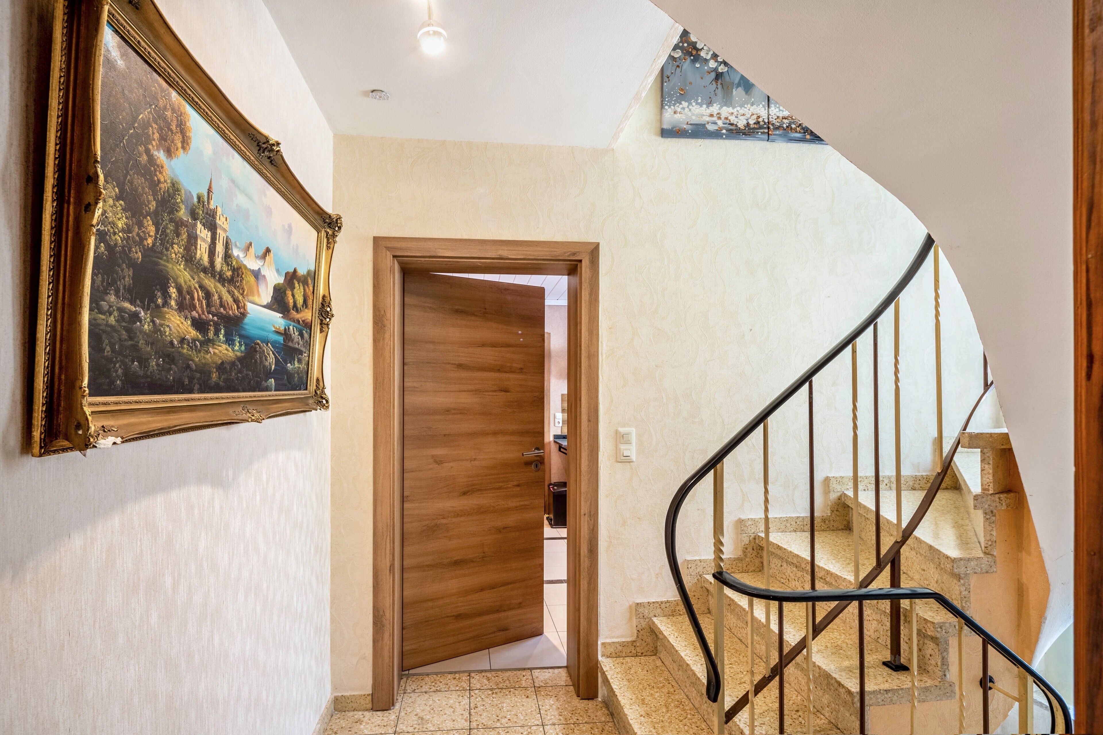 Ein Flur mit einer Holztür, einer Treppe mit Metallgeländer und einem Bild an der Wand.