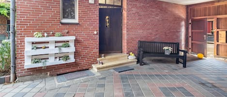 A brick building with a wooden bench, a white planter with plants, and a door with a small window.