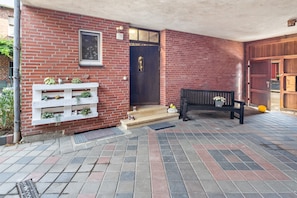 A brick building with a wooden bench, a white planter with plants, and a door with a small window.