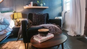 A modern living room with a dark wall, a sofa, a coffee table with a book, a lamp, and a window with curtains.