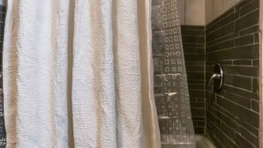 A bathroom with a shower curtain, tiled walls, and a showerhead.