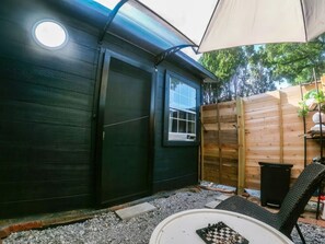 Un espace extérieur aménagé avec une table et des chaises, une clôture en bois et un bâtiment doté d’une fenêtre et d’une porte.