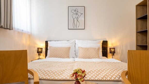 Una habitación de hotel con una cama, dos lámparas de noche, una obra de arte en la pared y un jarrón con flores sobre una mesa.