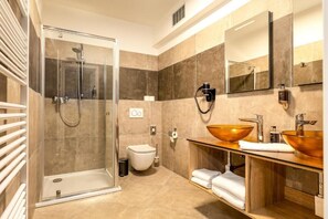A modern bathroom with a glass shower enclosure, a toilet, and a vanity with two copper sinks.
