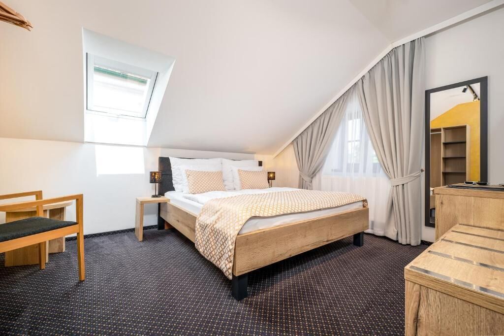 A bedroom with a bed, bedside tables, a desk, a mirror, and a window with curtains.