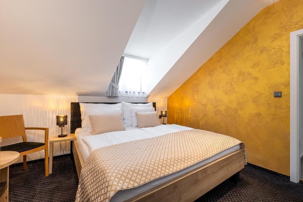 A bedroom with a bed, a chair, a nightstand, and a window.