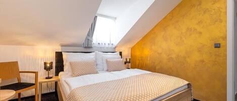A bedroom with a bed, a chair, a nightstand, and a window.