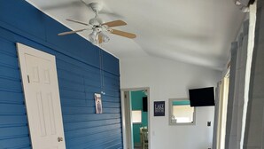 Une pièce avec un mur bleu, un ventilateur de plafond, un canapé en cuir marron, un plancher en bois et un téléviseur fixé au mur.