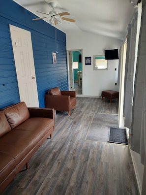 A room with a blue wall, a ceiling fan, a brown leather sofa, a wooden floor, and a television mounted on the wall.