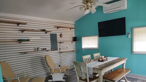 Une pièce comprenant une table à manger, des chaises, un ventilateur de plafond, un appareil de climatisation et un téléviseur fixé au mur.