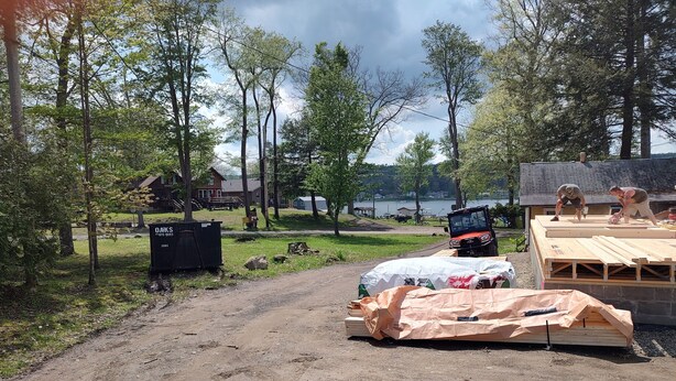 Un chantier de construction avec des planches de bois, une zone abritée et un chemin de terre.