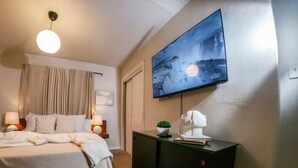 Une chambre d’hôtel avec un lit, des lampes de chevet, un téléviseur fixé au mur, une commode et une fenêtre avec des rideaux.