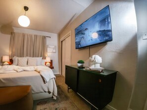 A hotel room with a bed, bedside lamps, a TV on the wall, a dresser, and a window with curtains.