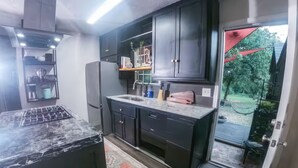 Une cuisine moderne avec des meubles de couleur sombre, une cuisinière à gaz et une porte-fenêtre coulissante donnant sur un espace extérieur.