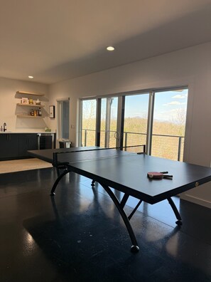 Eine moderne Küche mit Esstisch, einem Tischtennistisch und einem großen Fenster mit Blick auf Bäume.