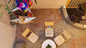A courtyard with a round table, four wooden chairs, a decorative plant, and a wall-mounted planter with colorful paper flowers. - Hotel La Casa de Mis Marias (Tlaquepaque)