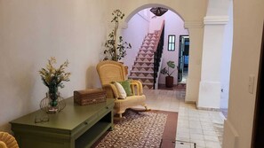 A hallway with a wicker chair, a green table, and a patterned rug.