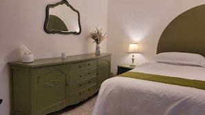 A bedroom with a bed, a dresser, a nightstand, a lamp, a mirror, and a vase with dried flowers.