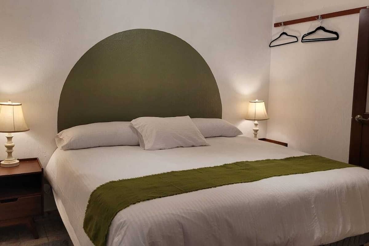 Un llit ben fet amb dos coixins, una manta verda i dues làmpades de nit.