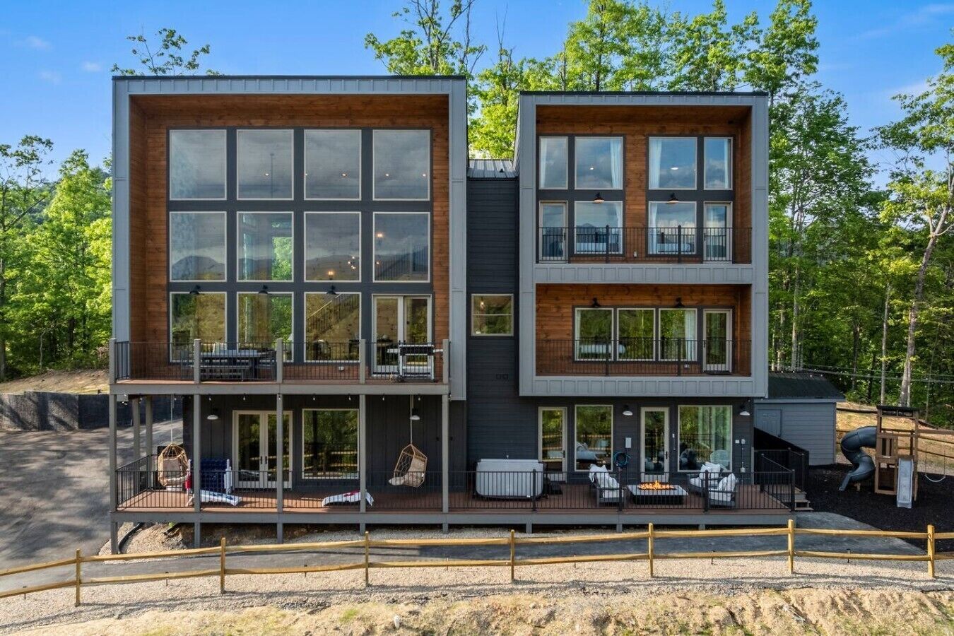 Une maison moderne à deux étages, dotée de grandes fenêtres, d’une terrasse et d’un espace salon extérieur.