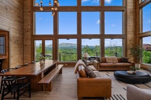 Ein geräumiges Zimmer mit großen Fenstern, einem Holzespeisetisch, einer Couch und Blick auf die Berge.