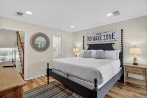 Ein Schlafzimmer mit einem Bett, einem Nachttisch, einer Lampe, einem Spiegel, einem Wandzeichen und einer Treppe.