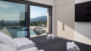 Een moderne hotelkamer met een groot bed, een televisie en een balkon met een zwembad en stoelen.