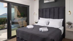 Een moderne hotelkamer met een groot bed, een schuifglazen deur naar een balkon, een wandairconditioner en een klein nachtkastje met een bloemenvaas.