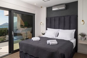 Ein modernes Hotelzimmer mit einem großen Bett, einer Schiebetür zu einem Balkon, einer Wandklimaanlage und einem kleinen Nachttisch mit einem Blumenstrauß.