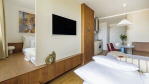 A hotel room with a bed, a TV mounted on the wall, a wooden cabinet, a desk with a chair, and a small table with a plant. - Top floor studio with balcony and smart design (Hlavní město Praha)