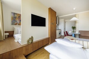 Ein Hotelzimmer mit einem Bett, einem an der Wand montierten Fernseher, einem Holzschrank, einem Schreibtisch mit Stuhl und einem kleinen Tisch mit Pflanze.