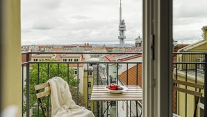 A balcony with a chair and table, a cityscape view, and a tower in the distance. - Top floor studio with balcony and smart design (Hlavní město Praha)