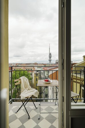 Ein Balkon mit Stuhl und Tisch, Blick auf eine Stadtlandschaft und ein Turm in der Ferne.