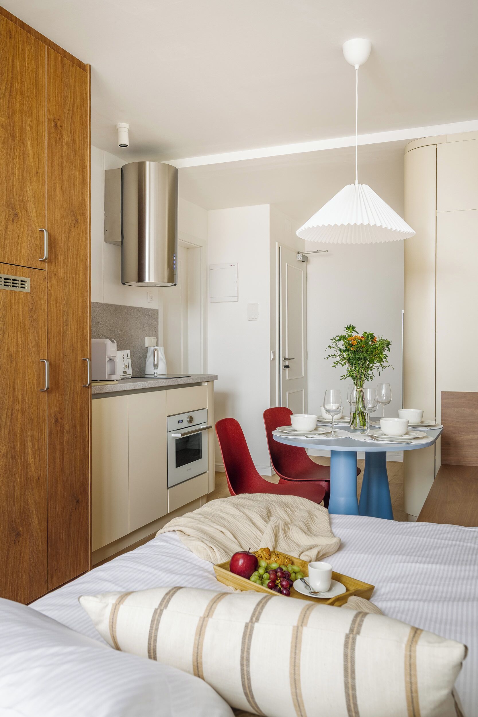 Et moderne hotelværelse med tekøkken, spiseplads med bord og stole, samt seng med frugtfat og kop.
