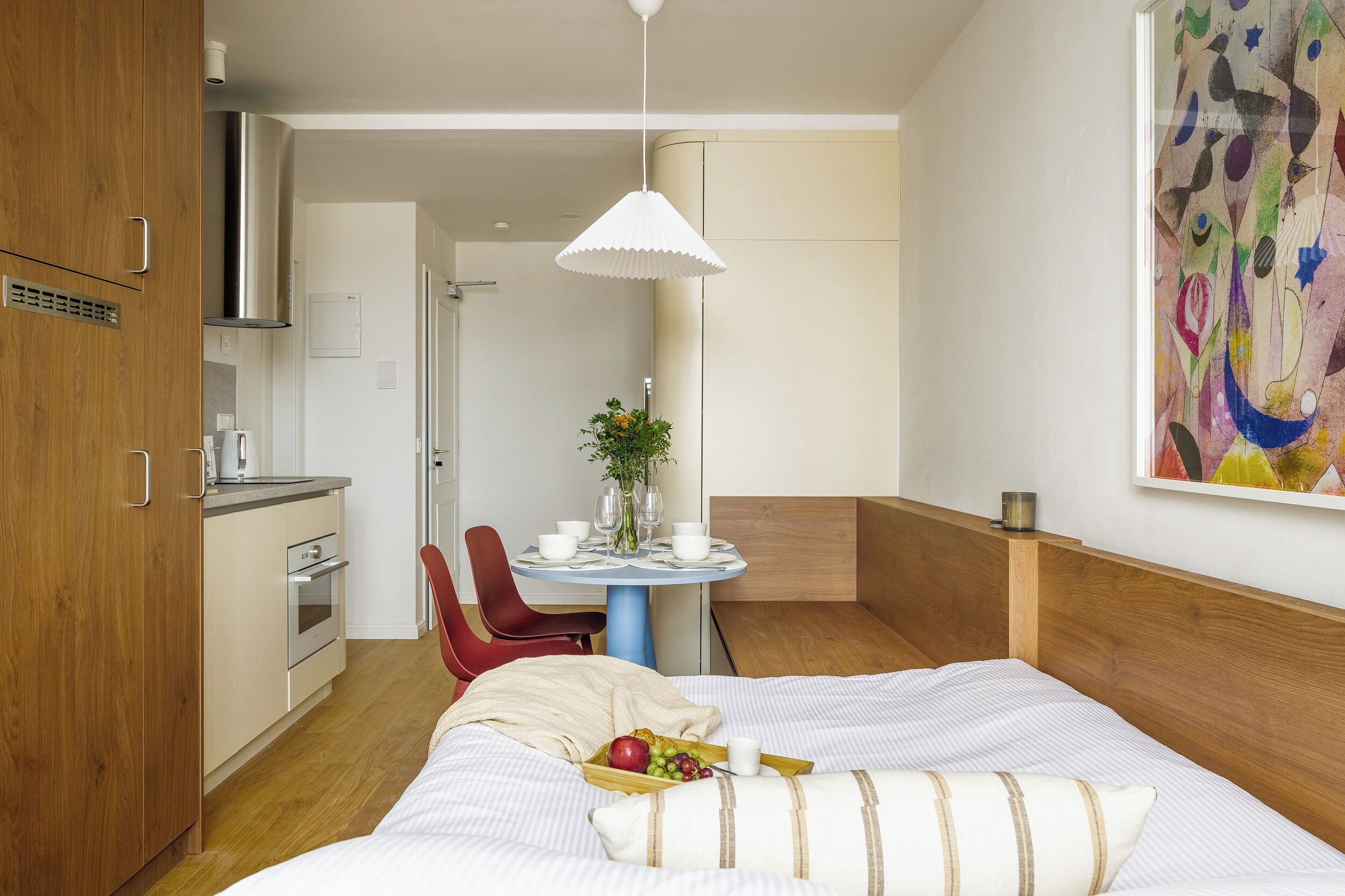 Une chambre d’hôtel comprenant un lit, une table à manger avec des chaises, un coin cuisine et un tableau au mur.